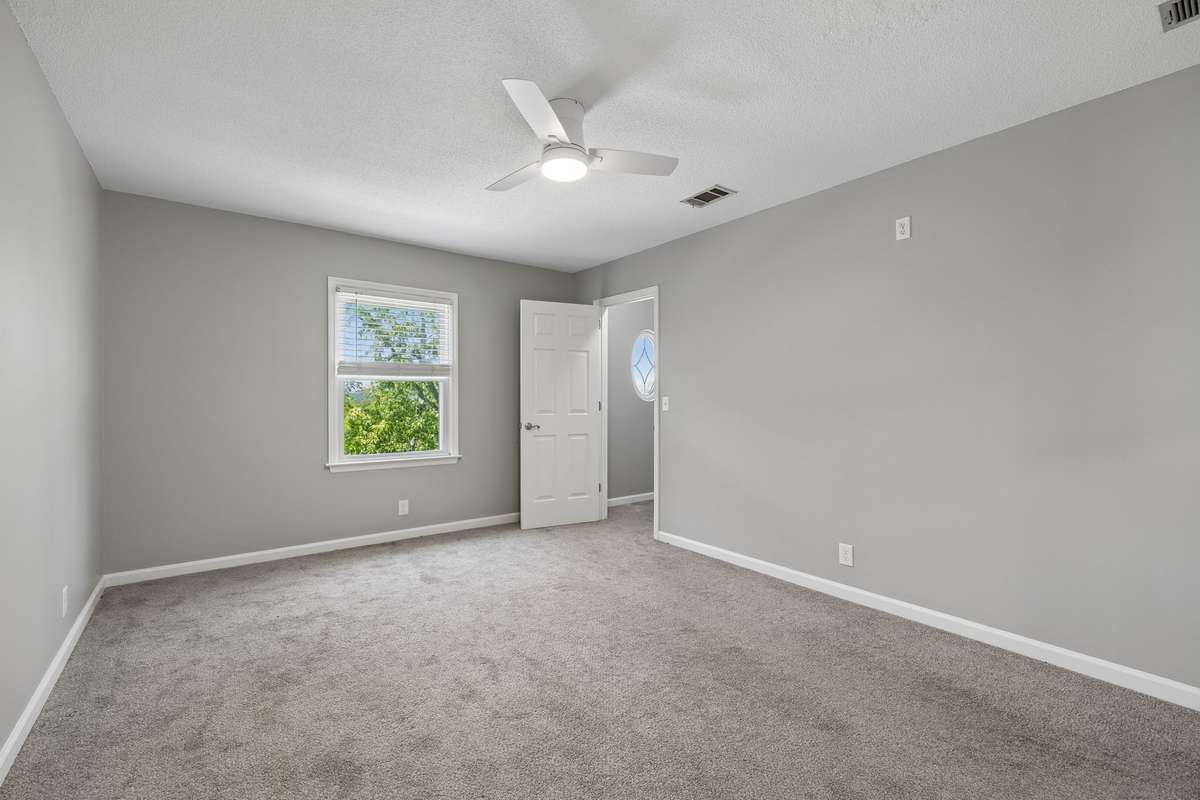 Another view of the primary bedroom facing toward the walk-in closet. Note the oval window in the walk-in closet that gives natural light inside the closet and, also, is a lovely architectural feature when viewed outside the home.