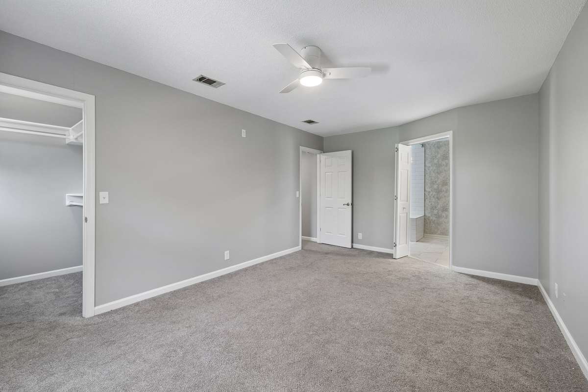 A view of the primary bedroom from the front of the house looking toward the primary bathroom and (on top center of photo) hallway entrance. The ceiling fans with tasteful lighting have been installed in all three bedrooms as well as the living room.