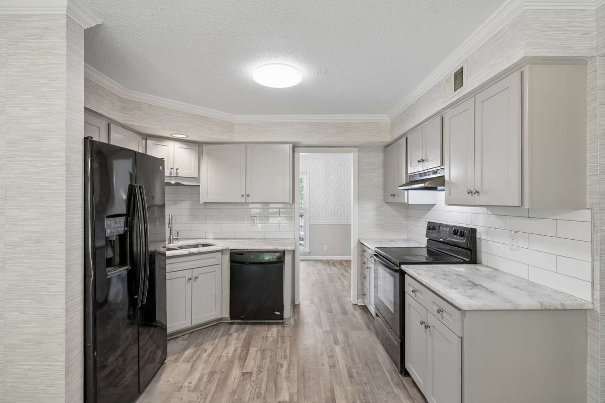 A view of the kitchen looking into the dining room at far, center of photo.  Note the new wallpaper to left and above cabinets.