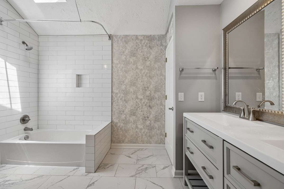 The beautiful primary bathroom has a double vanity and a tub/shower combo with subway tile to the ceiling.  It has been freshly painted and features designer wallpaper.