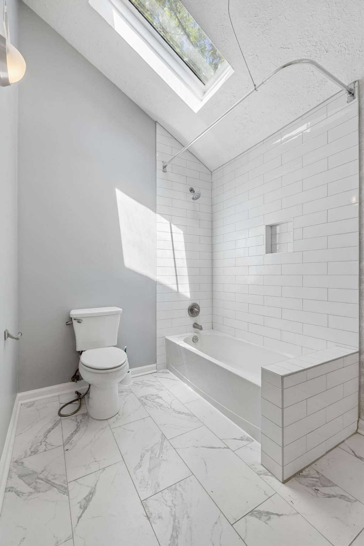 A view of the primary bath's tub/shower, commode and, above, a skylight allowing natural light into the room.