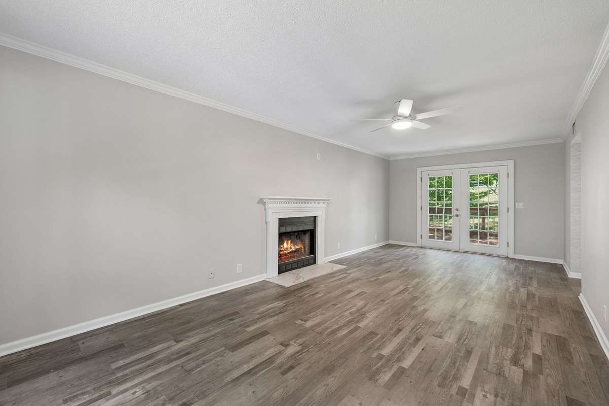 A view of the living room from the front hall.  New ceiling fan. New luxury vinyl flooring. French Doors. Working fireplace.