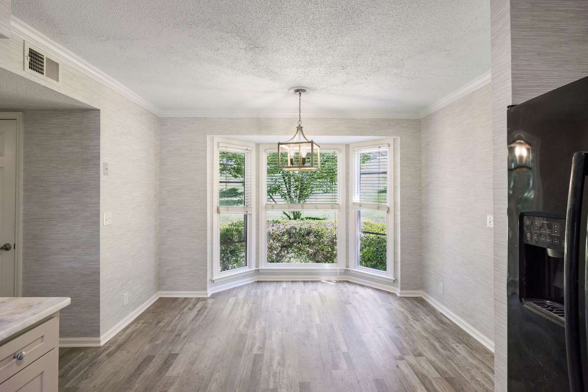 A view of the kitchen from the dining room.  Large, eat-in breakfast nook. Bay window offering beautiful views of backyard. The entire kitchen, breakfast nook and hallway (to the left in photo) have new wallpaper.