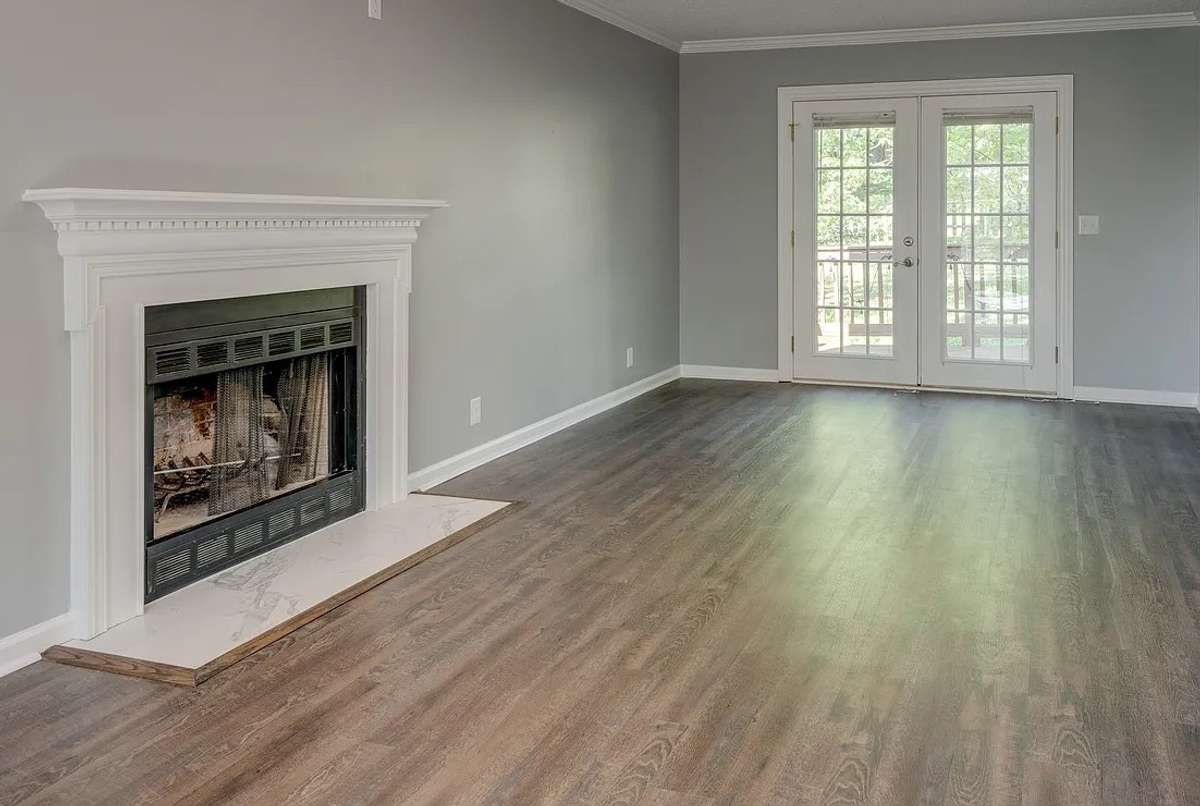 A closer view of the living room. The home's brand new luxury vinyl flooring shows beautifully in the living room. Note the handsome fireplace and French Doors.