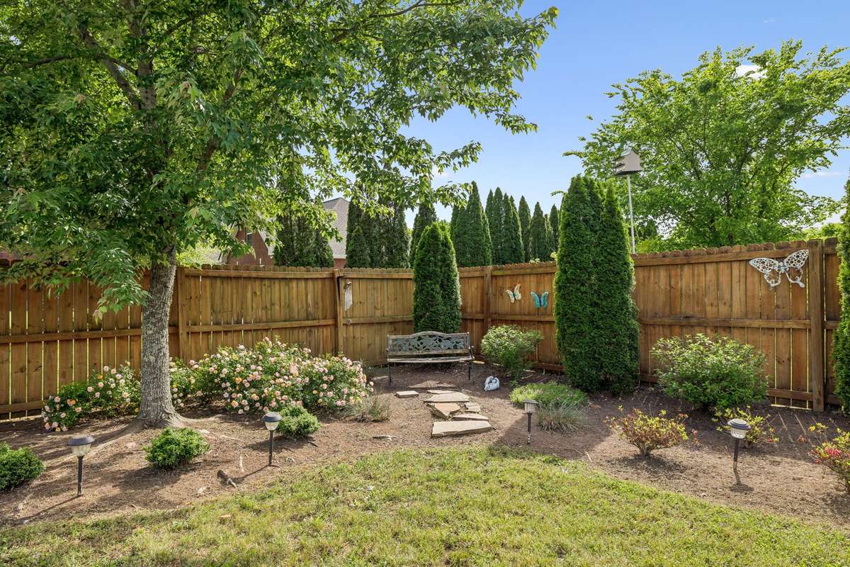 Landscaped backyard corner with shade, flowers, and bench seating.
