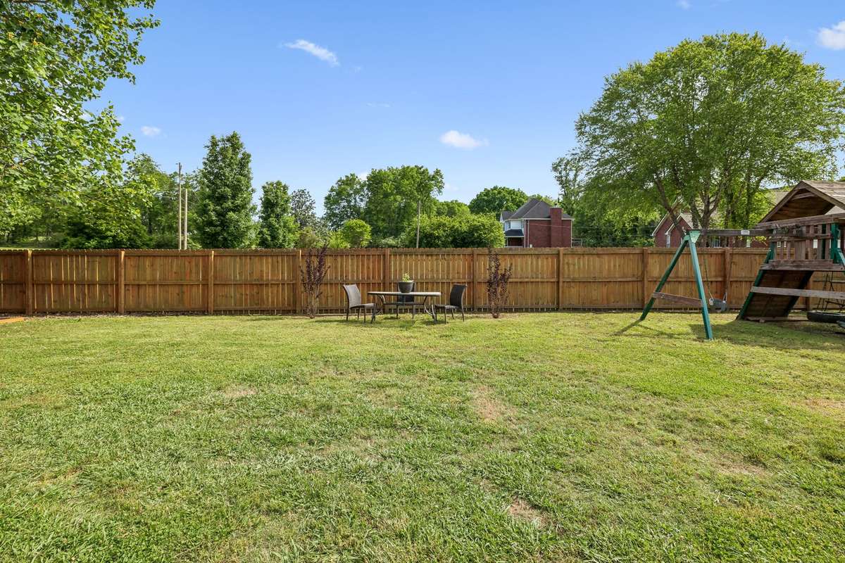 Fenced backyard with playset and outdoor seating area.