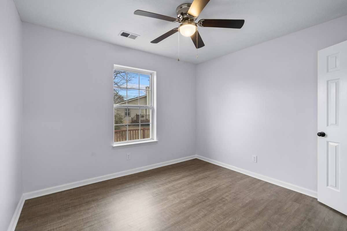 Bedroom three also features luxury vinyl flooring, a serene view overlooking the deck, a ceiling fan, and a full closet—making it a tranquil and stylish space for guests or family.
