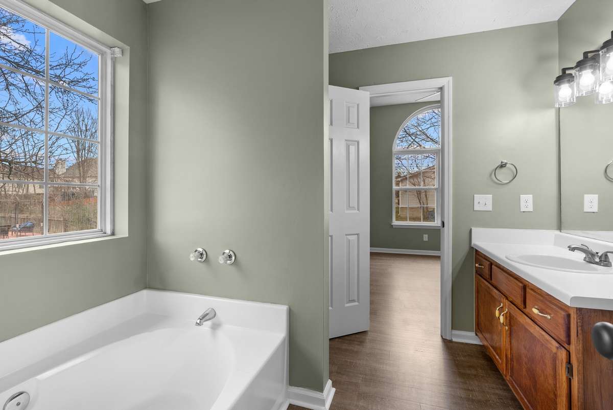 A large window illuminates the soaking tub, while a separate shower and luxury vinyl flooring complete this space.