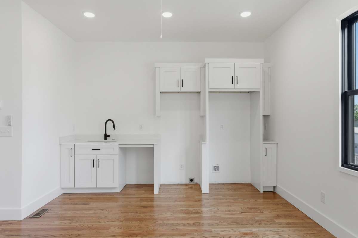 The kitchenette includes a sink, white cabinetry, and quartz countertops, along with a dedicated space for a refrigerator and laundry hookups.
