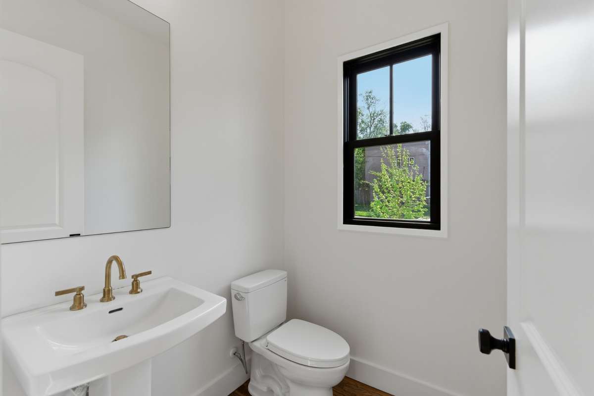 Tucked conveniently between the living area and kitchen, the powder room features a classic pedestal sink and elegant gold fixtures.