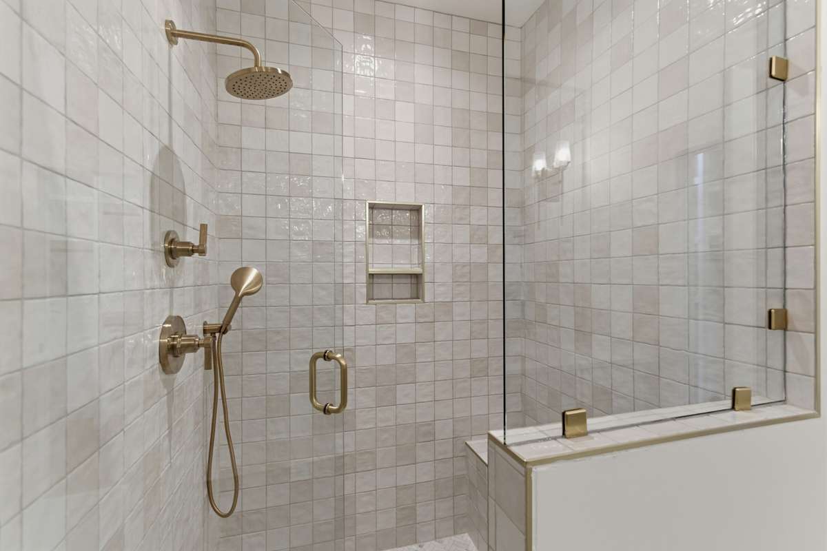 The walk-in shower is a true centerpiece, featuring floor-to-ceiling zellige-style tile, a rainfall showerhead, and a built-in bench.
