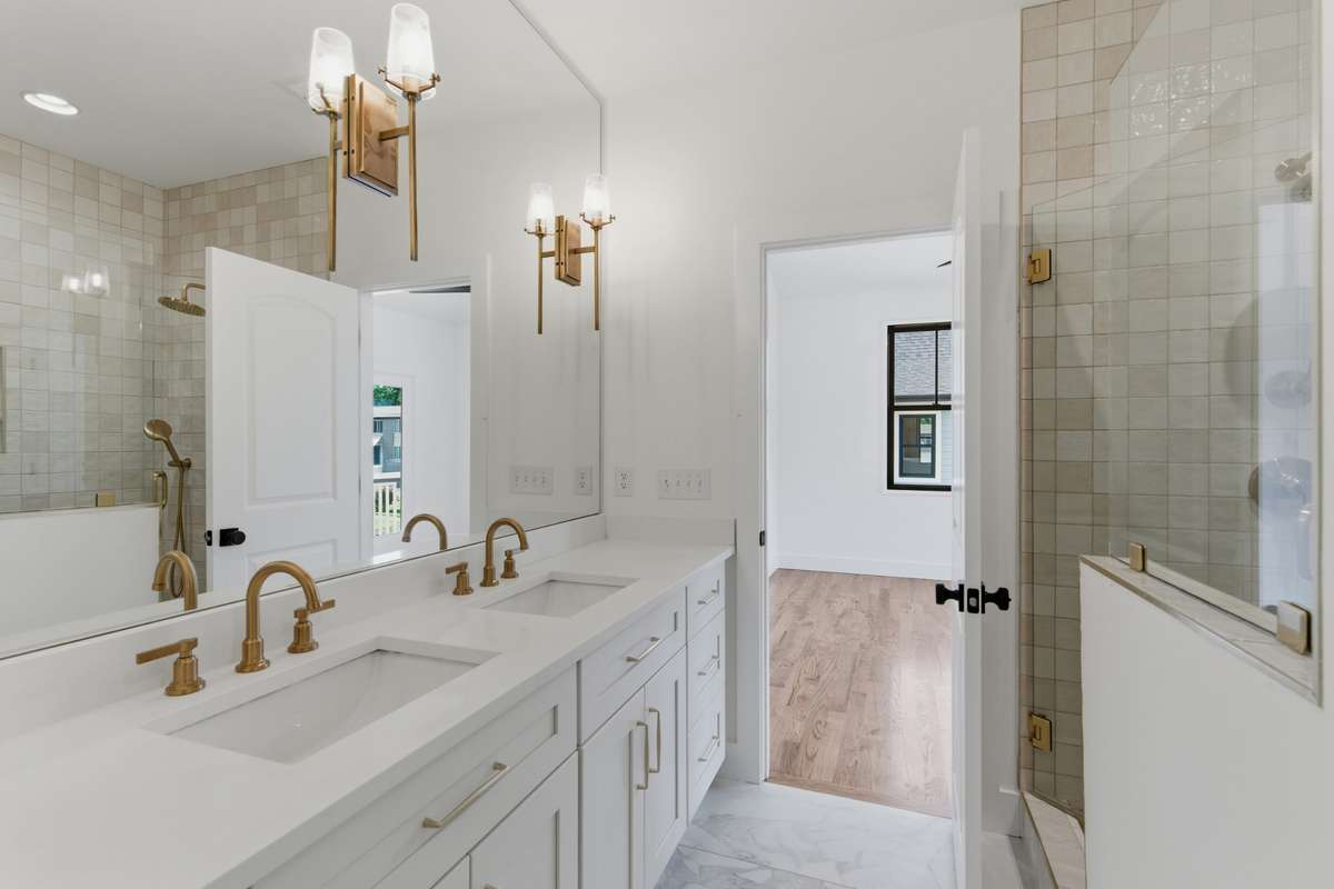 Elegant gold fixtures and modern wall sconces pair perfectly with the clean white cabinetry and marble-style flooring.