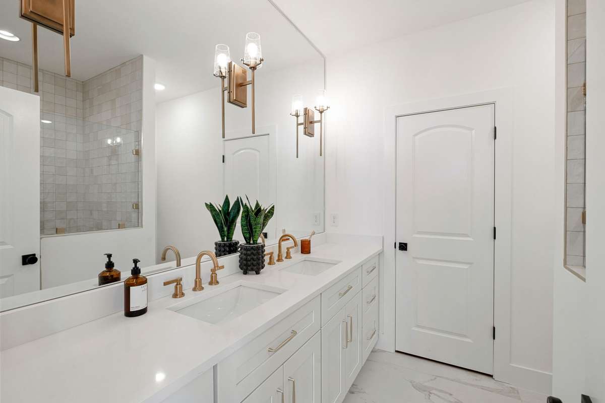 The attached bath features a quartz vanity with gold finishes, elegant lighting, and a mirror that stretches all the way to the ceiling.