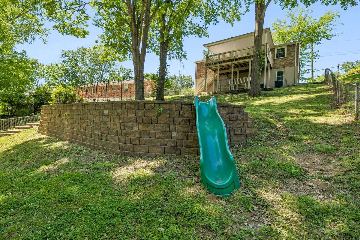 Massive fenced backyard with mature trees, plenty of space to play or entertain, and a built-in slide for added fun.