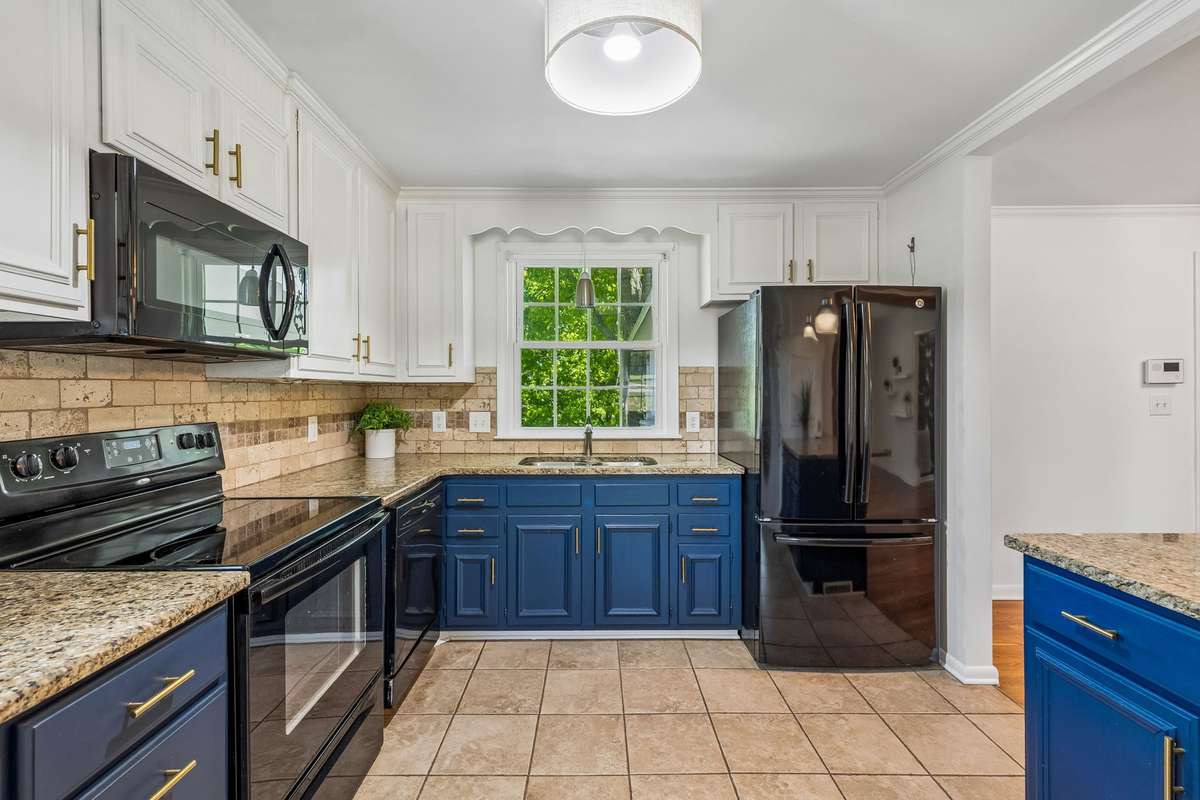 Updated kitchen with granite countertops, two-tone cabinetry, and black appliances, filled with natural light.