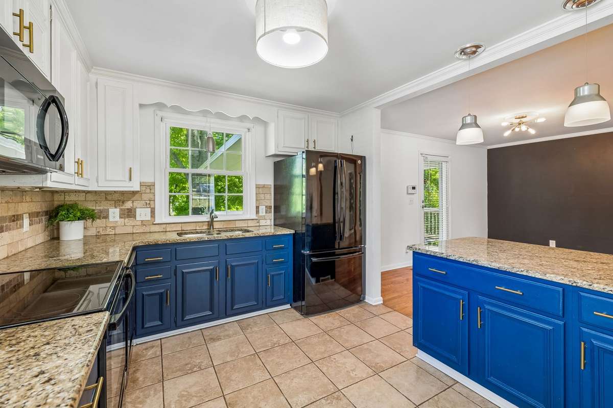Updated kitchen with granite countertops, two-tone cabinetry, and black appliances, filled with natural light.