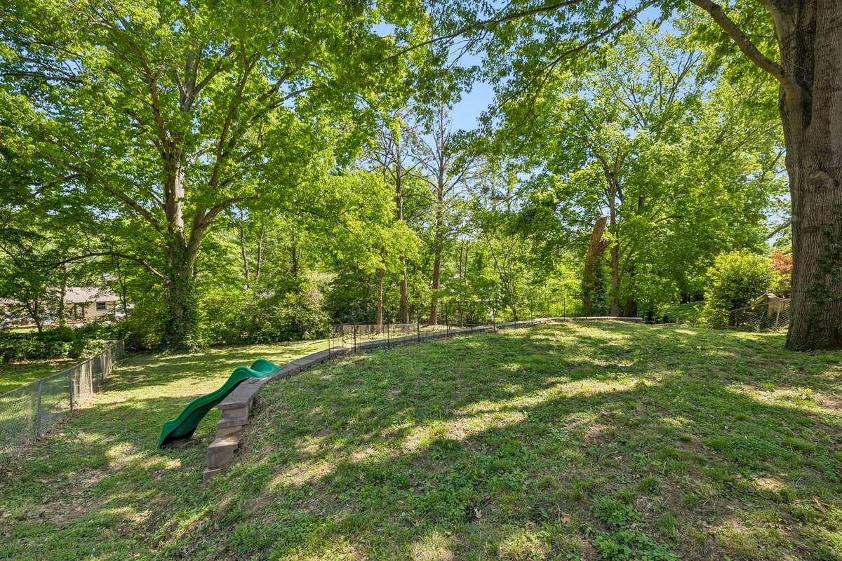 Massive fenced backyard with mature trees, plenty of space to play or entertain, and a built-in slide for added fun.