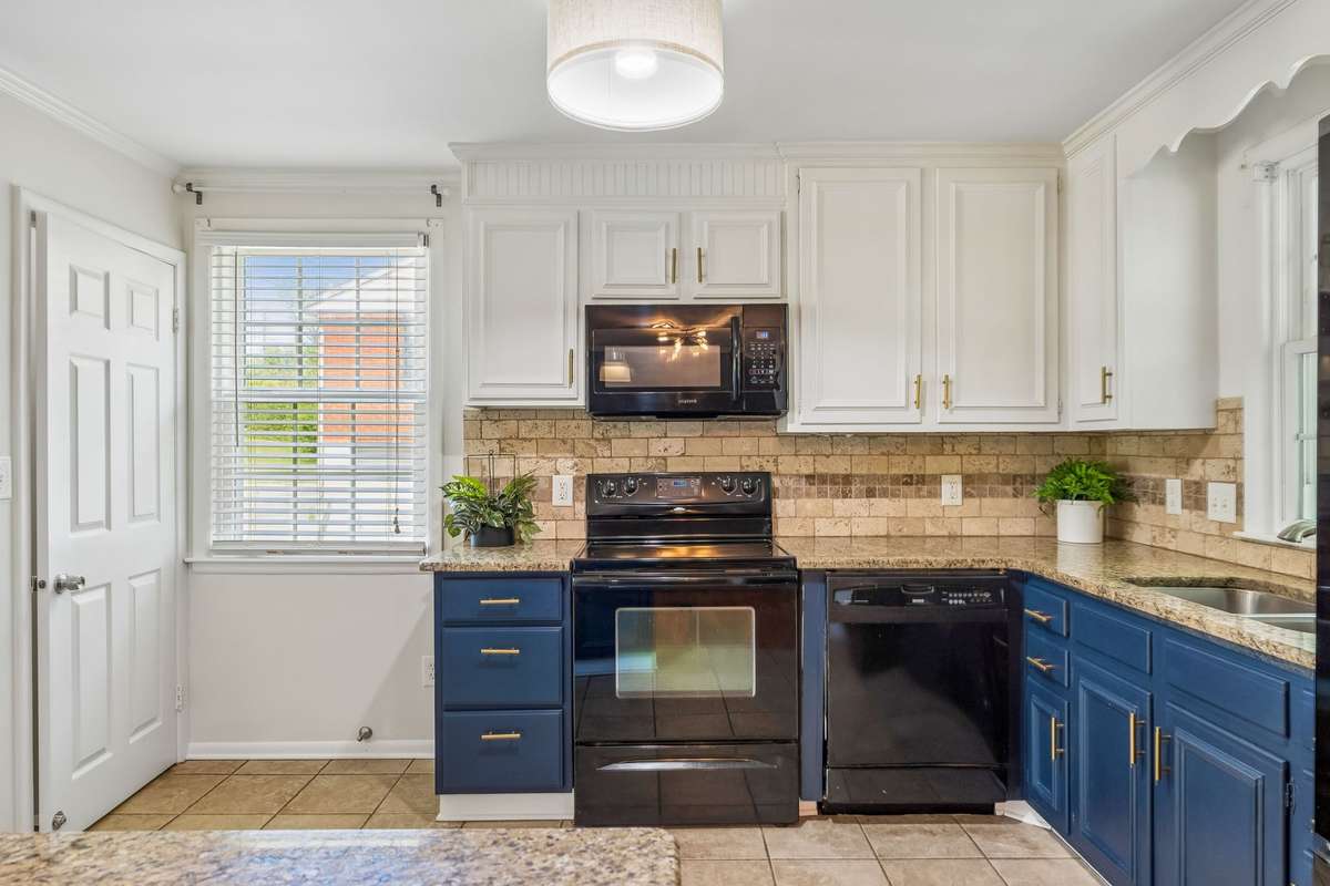 Updated kitchen with granite countertops, two-tone cabinetry, and black appliances, filled with natural light.