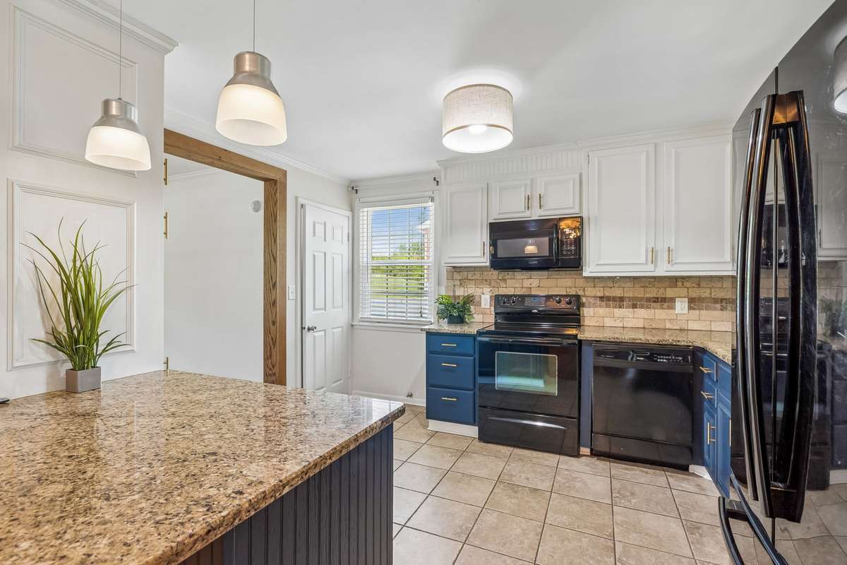 Updated kitchen with granite countertops, two-tone cabinetry, and black appliances, filled with natural light.