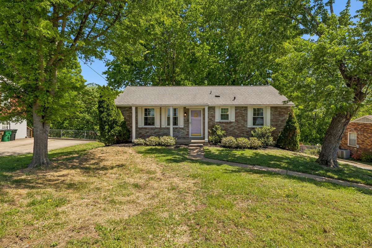 Charming brick exterior with mature trees, welcoming front entry, and spacious front yard.