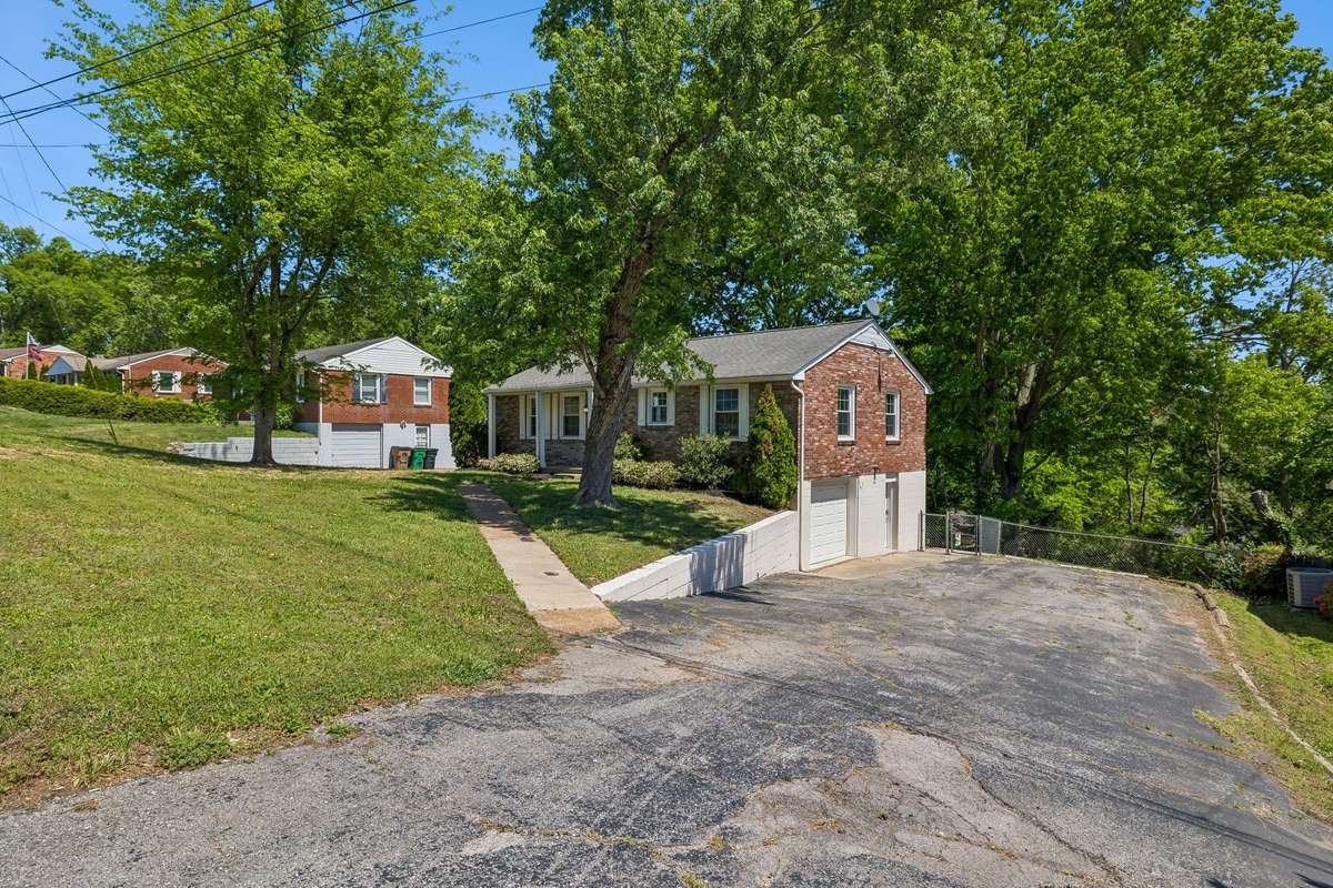 Spacious driveway with one-car garage, mature trees, and sloped lot offering added privacy.
