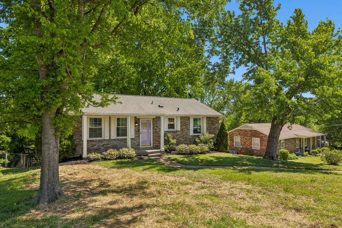 Charming brick exterior with mature trees, welcoming front entry, and spacious front yard.