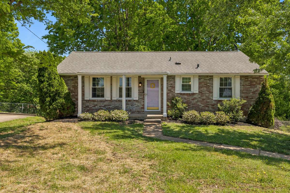 Charming brick exterior with mature trees, welcoming front entry, and spacious front yard.