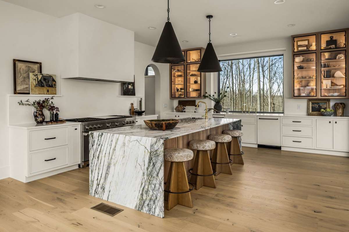 Gourmet kitchen featuring a dramatic marble island with waterfall edges, custom cabinetry, premium appliances, and abundant natural light, thoughtfully designed for both everyday living and elevated entertaining.