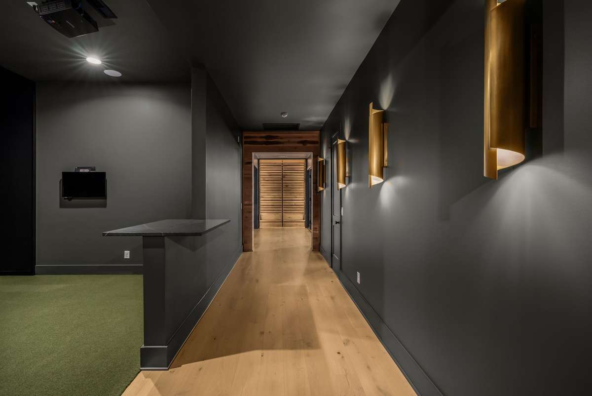 A moody downstairs hallway illuminated by sculptural sconces, leading to a private golf simulator experience.