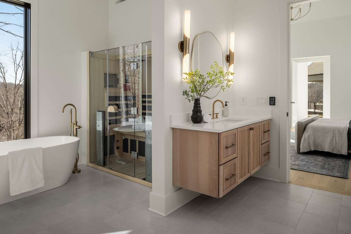 Primary bathroom featuring a freestanding soaking tub, glass-enclosed sauna, floating vanity, and refined finishes designed to create a spa-like retreat.