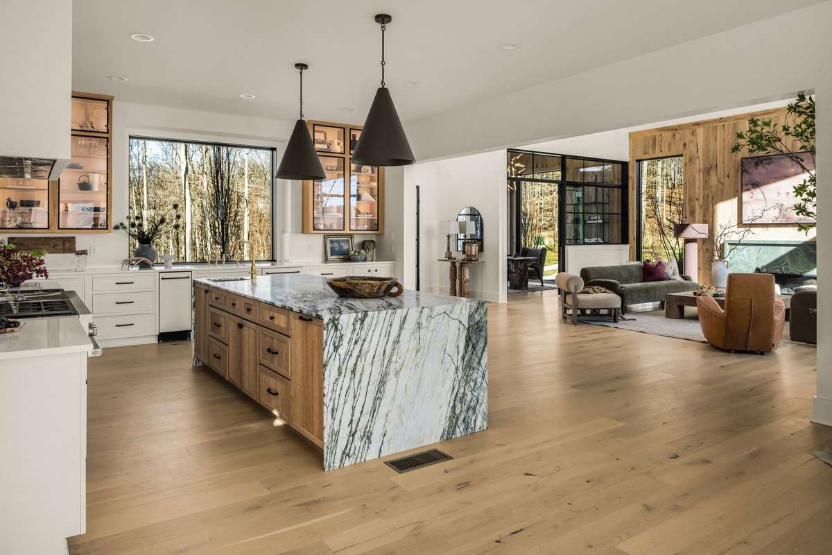 Wide kitchen perspective highlighting the dramatic marble island, professional-grade gas range, and seamless connection to the main living areas, all framed by expansive windows and natural light.