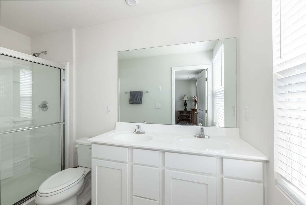 Attached primary bathroom with beautiful white cabinetry, double sinks and walk in shower