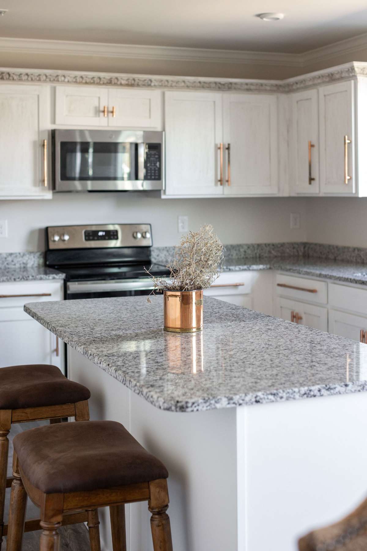 Beautiful white kitchen features an island, granite countertops, crown molding, updated copper hardware, and stainless steel appliances