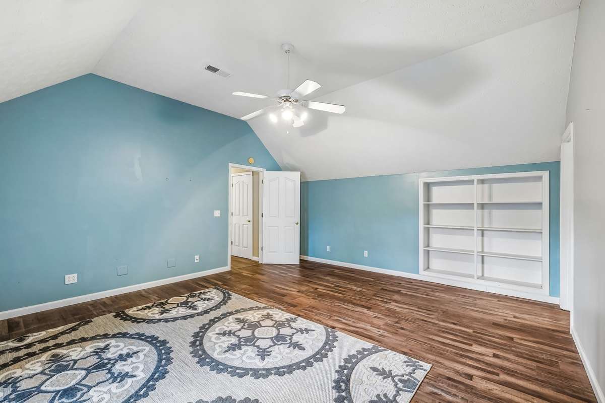 Vaulted ceiling with a ceiling fan and built-in shelving that spans the width of the wall, good spot for books or display items.