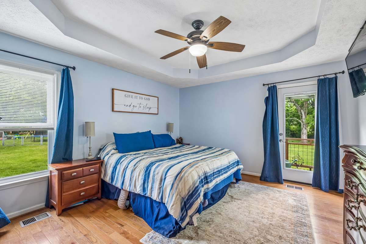 Primary bedroom on the main level with tray ceiling and hardwood floors, plus a direct door to the backyard deck.