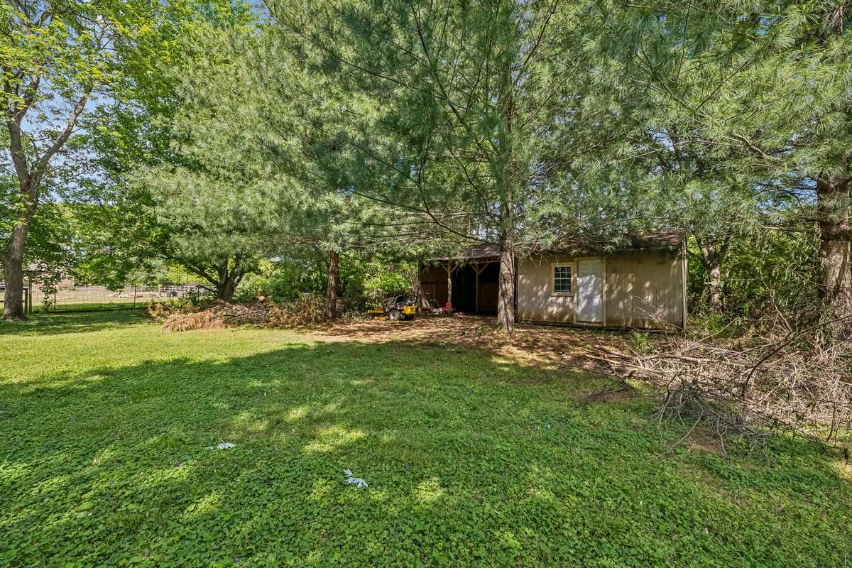 The detached workshop sits tucked under mature trees with additional finished space above for a home office or storage.