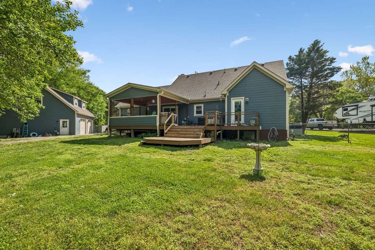 Fenced backyard stretches out from the covered deck with level grass and mature trees for plenty of shade