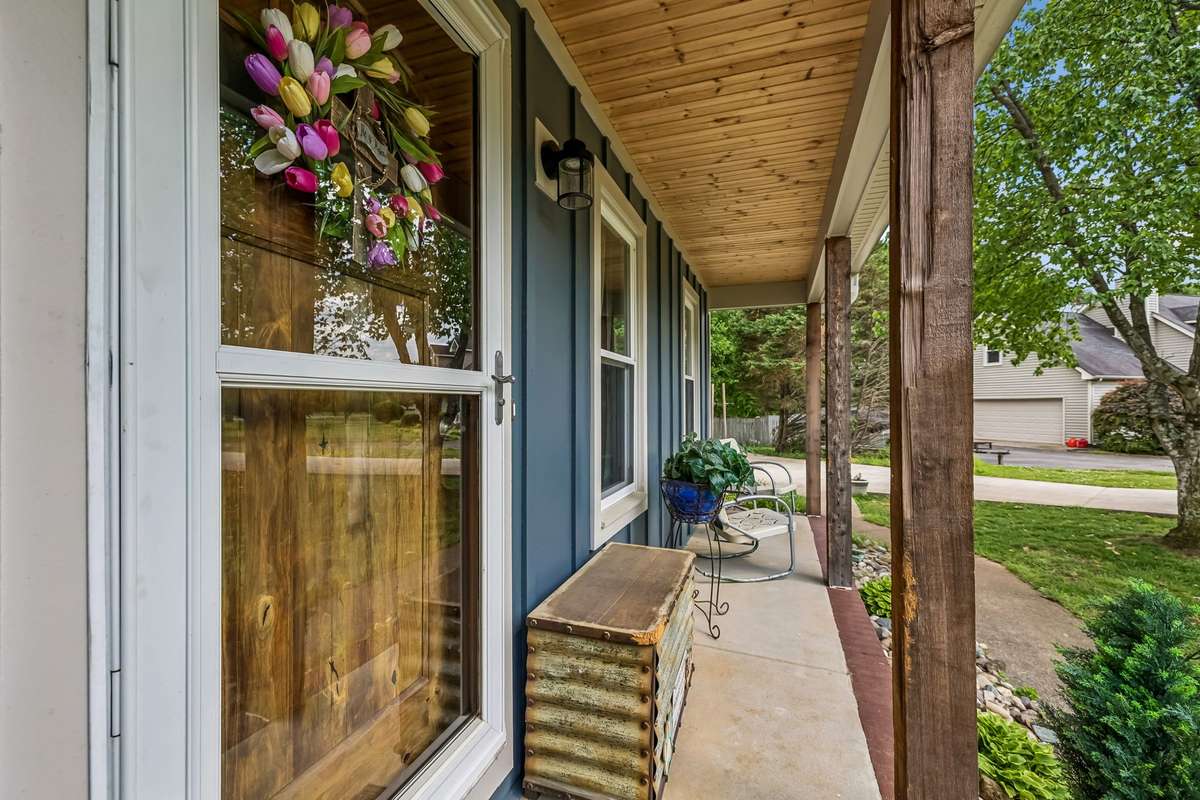 Covered porch runs the full width of the front with wood ceiling overhead and stone columns anchoring each end.