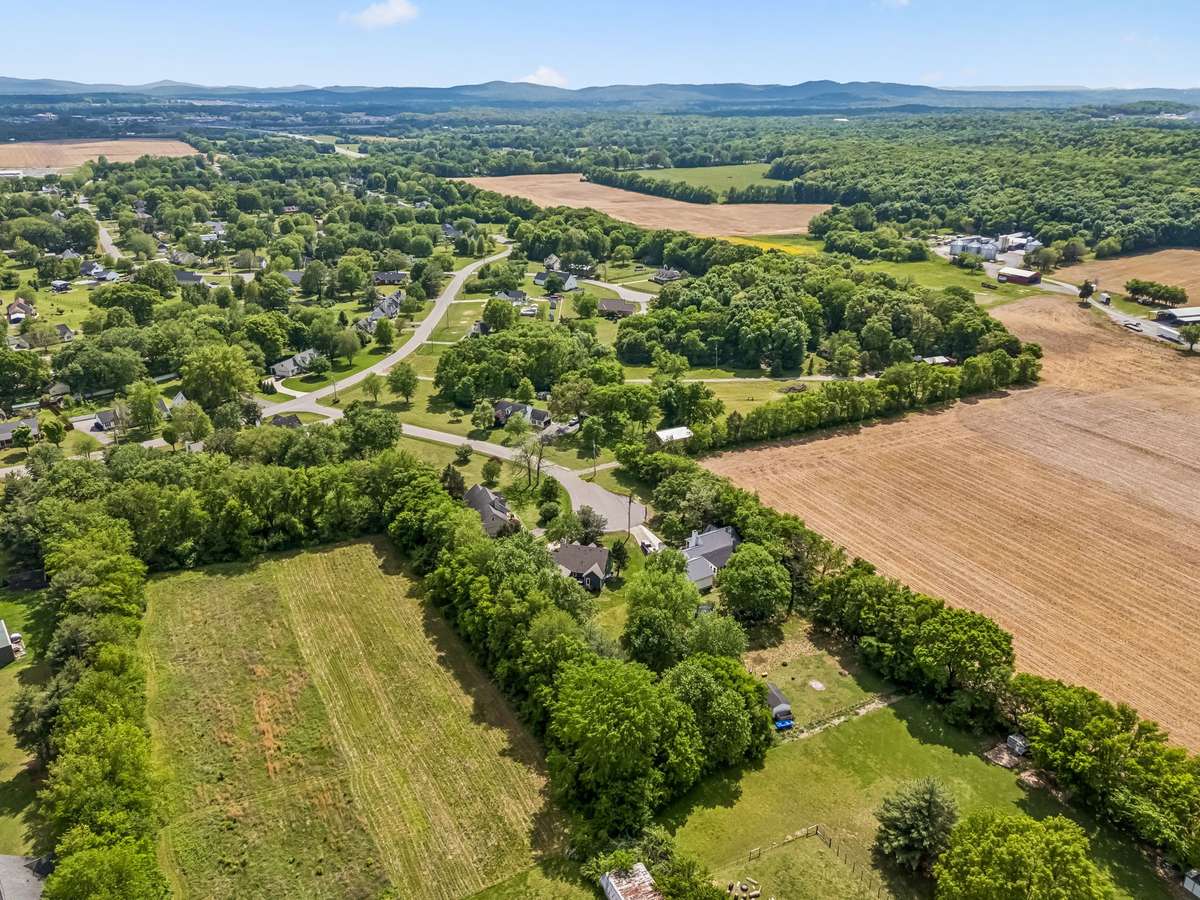 Aerial view shows this home's location on a quiet cul-de-sac with mature trees, open farmland nearby, and the city stretching toward the horizon.