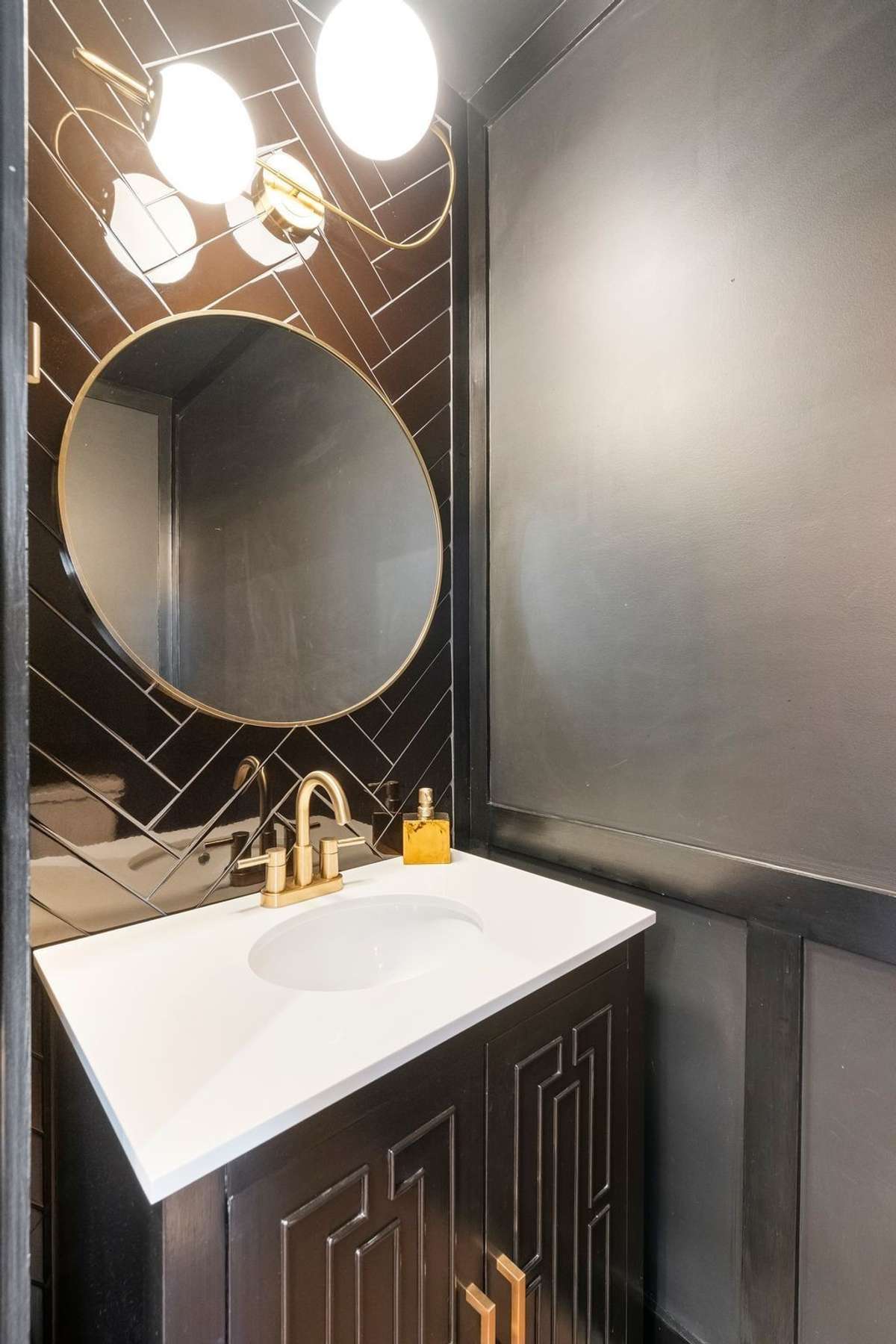 Chic powder room featuring black tile, gold accents, and a designer vanity.
