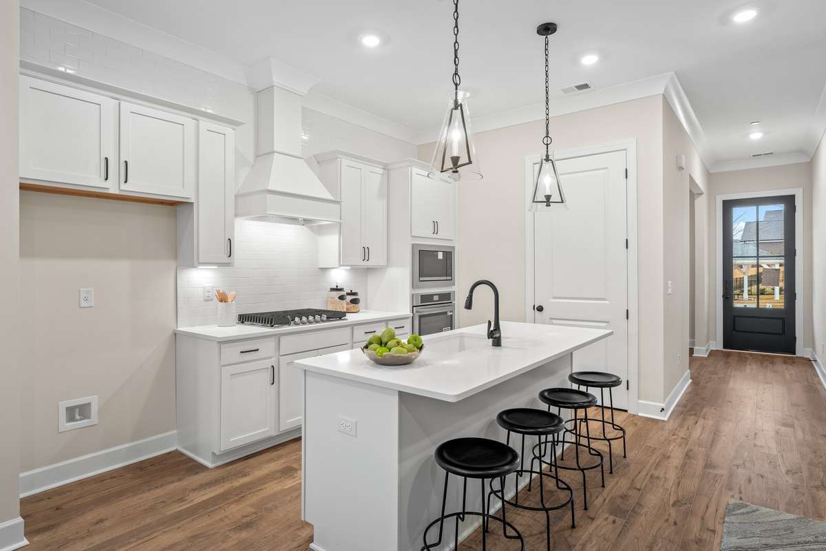 Lovely kitchen with decorative hood over gas cooktop, ovens built in cabinet and large island.