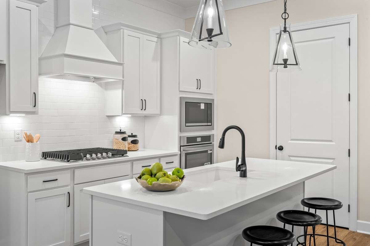 Gorgeous chef's kitchen with pantry, quartz island, GAS cooktop and ovens built into wall cabinet plus decorative vent hood and tile backsplash