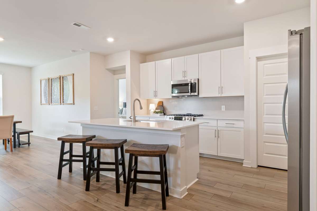 Open kitchen featuring a large island, white cabinetry, and seamless flow into the living and dining areas.