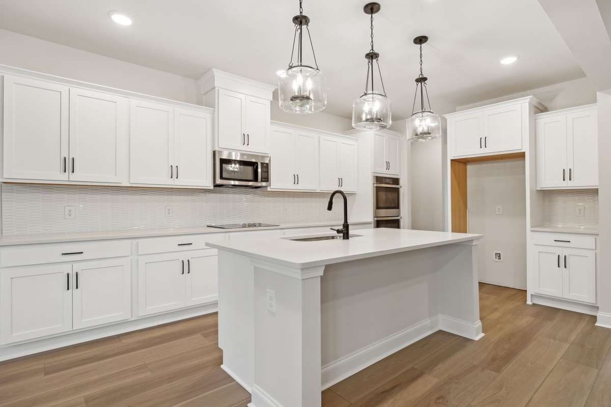 This stunning kitchen showcases white cabinetry, quartz countertops, a white tile backsplash, and stylish pendant lighting over the island. The perfect blend of modern design and functionality, ideal for both everyday living and entertaining.