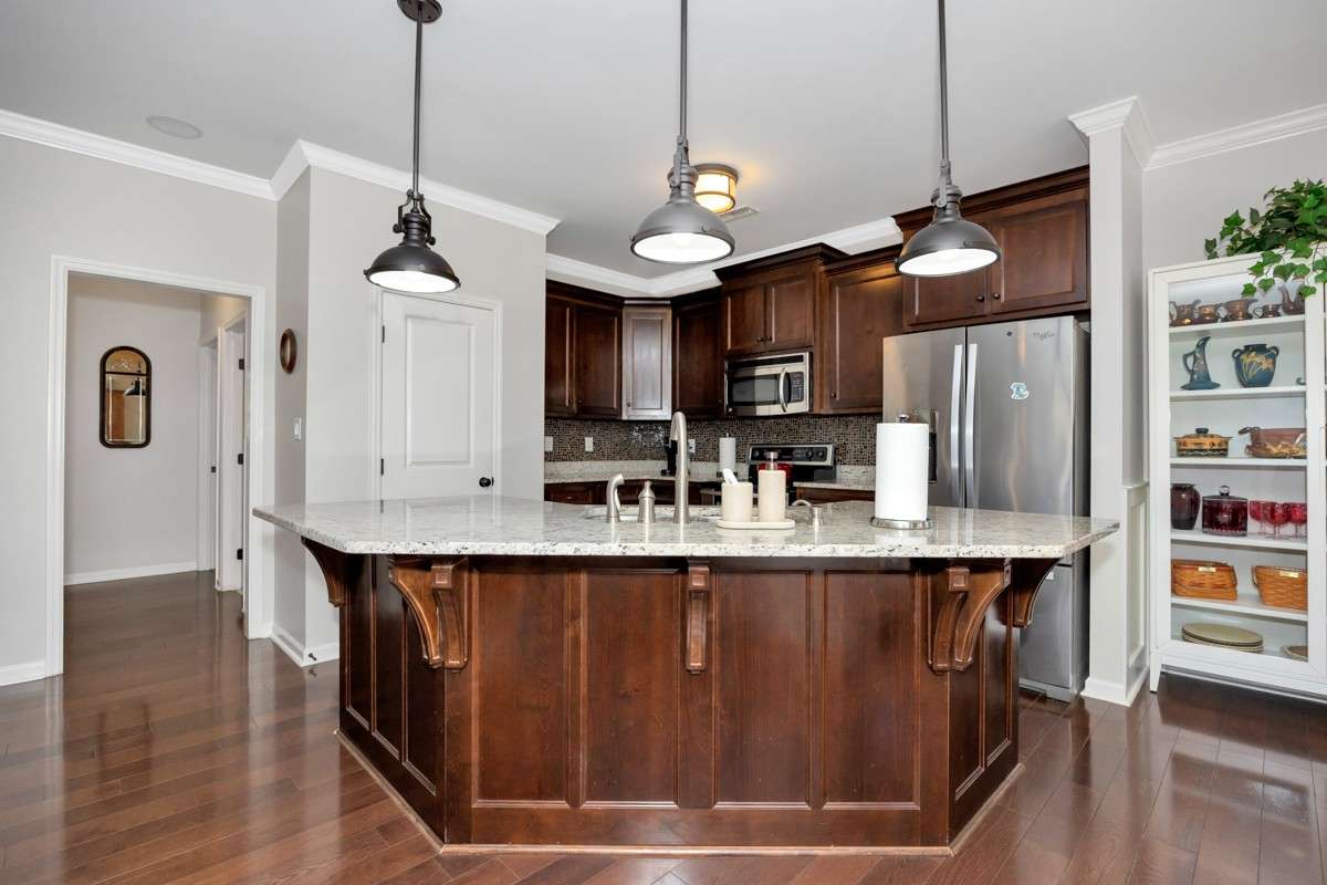 Kitchen- wood flooring, granite countertop, crown molding, bar seating, pantry, tile backsplash, stainless appliances:  refrigerator, microwave, stove, oven
