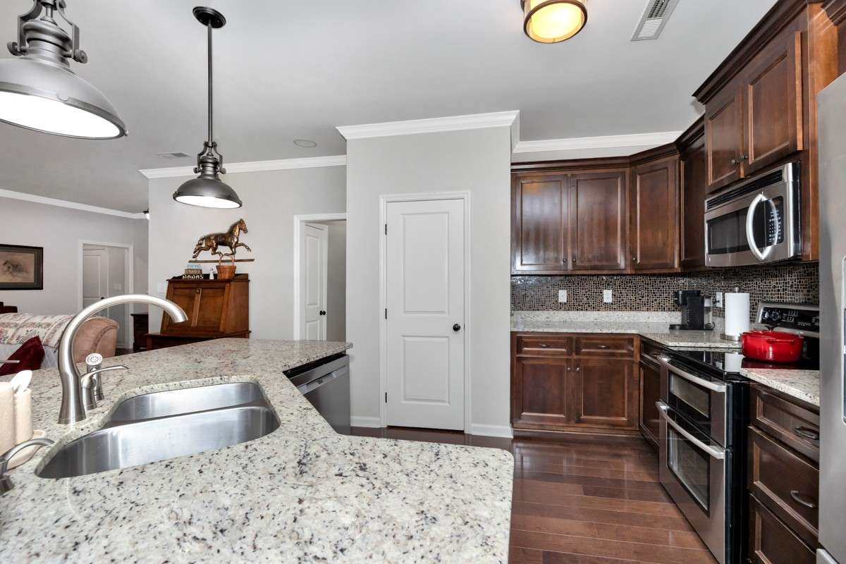 Kitchen- wood flooring, granite countertop, crown molding, bar seating, pantry, tile backsplash, stainless appliances:  refrigerator, microwave, stove, oven
