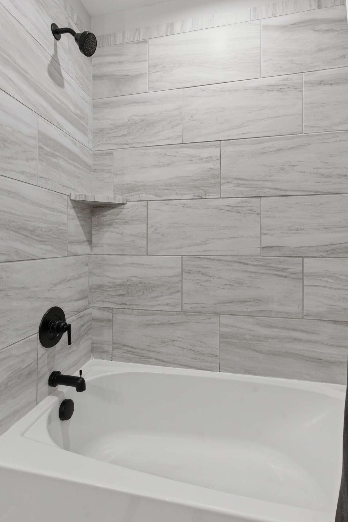 Tub and shower combo with elegant tile work and black fixtures for a striking, modern contrast!