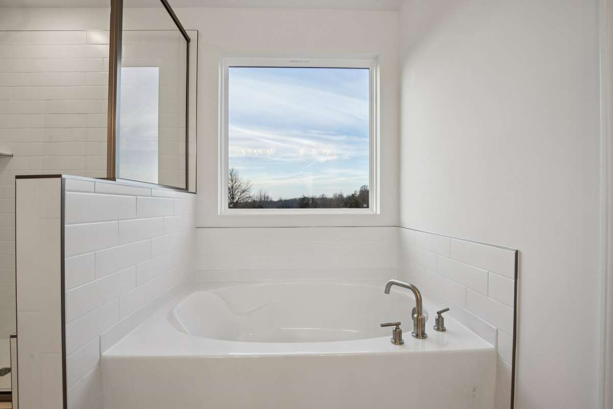 Unwind in your luxurious garden tub, surrounded by tile that adds a touch of sophistication. Perfect for relaxing, this tub offers a spa-like experience right at home, complemented by a picture window letting is natural light for a serene atmosphere.
