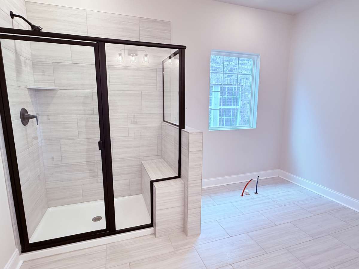 The primary bathroom showcases tile flooring and a fully tiled shower with a built-in bench, offering both comfort and convenience. A freestanding tub will be added soon, completing the space as an ideal retreat to relax and recharge.