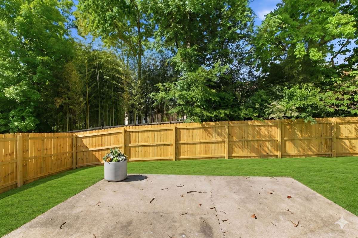 Large concrete patio overlooking the fully fenced, tree-lined private backyard.